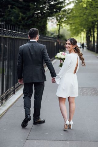 Baiser romantique d'un couple de mariés au milieu d'une rue parisienne, avec une architecture haussmannienne en arrière-plan