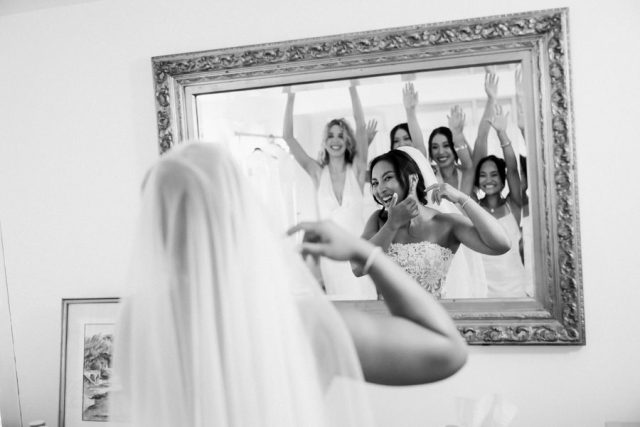 La mariée, de dos, s'observe dans le miroir lors de ses préparatifs, photographie en noir et blanc.