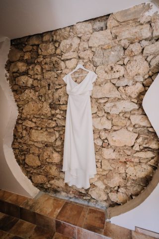 La robe de mariée suspendue contre un mur en pierre rustique en Provence.
