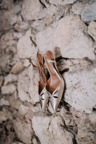 Détail des chaussures de la mariée posées sur un muret en pierre.