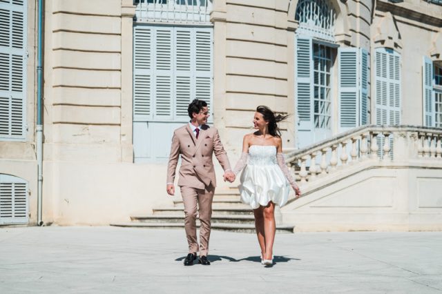 Les jeunes mariés marchent avec assurance sur la grande esplanade devant le bâtiment de la mairie de Marseille.