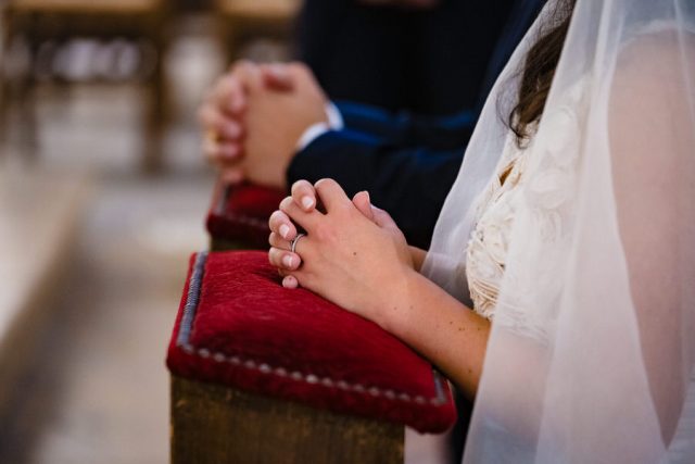 Mains de la mariée posées sur le prie-Dieu rouge pendant le recueillement à l'église.