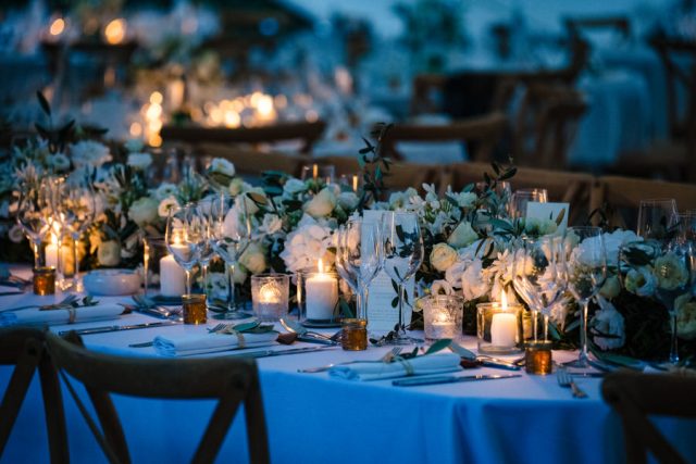 Longues tables de banquet illuminées de bougies pour un dîner de mariage féérique en extérieur.