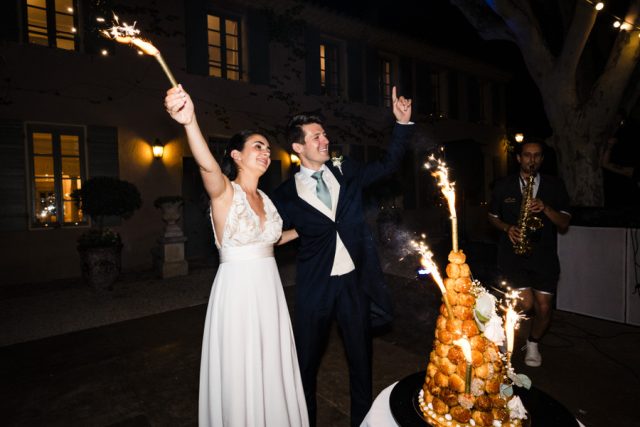 Les mariés posent souriants derrière leur pièce montée en croquembouche illuminée de fontaines lumineuses.