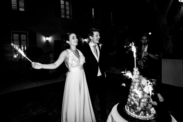 Photographie en noir et blanc des mariés célébrant l'arrivée traditionnelle du gâteau de mariage.