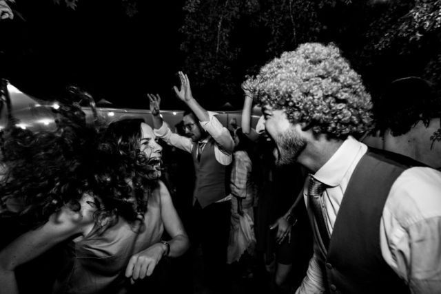 Soirée de mariage déjantée, le marié porte une perruque humoristique sur la piste de danse.