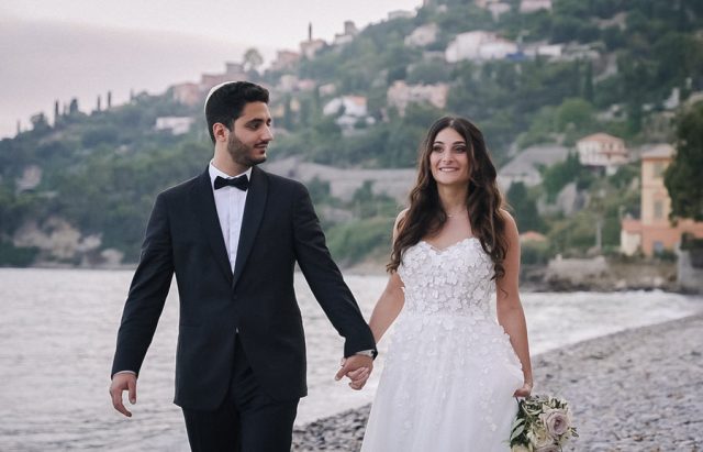 Les mariés marchent main dans la main sur une plage de galets lors de leur mariage en Italie.