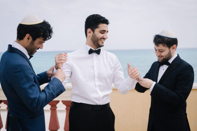 Les amis du marié, portant la kippa, l'aident à enfiler sa chemise lors des préparatifs.