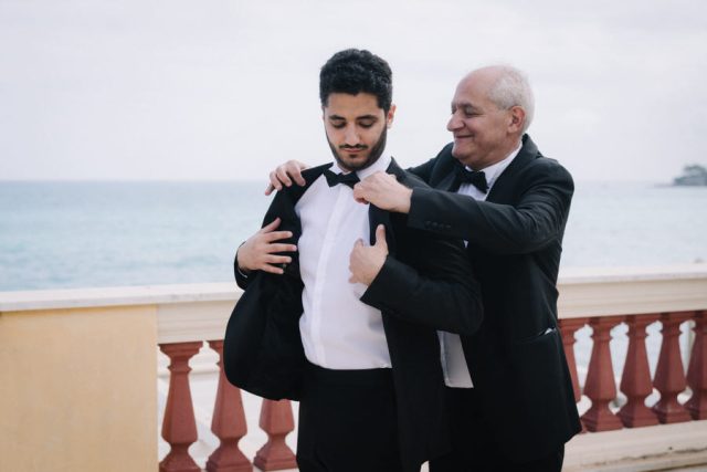 Le marié enfile sa veste de costume sombre aidé par son père avant la cérémonie de mariage.