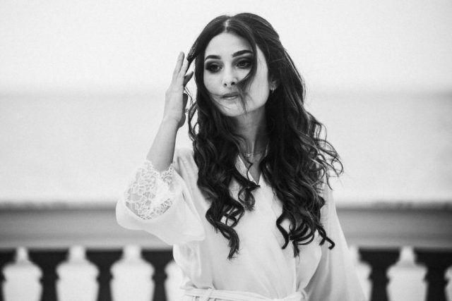 Portrait en noir et blanc de la mariée au naturel ajustant ses cheveux avant d'enfiler sa robe.