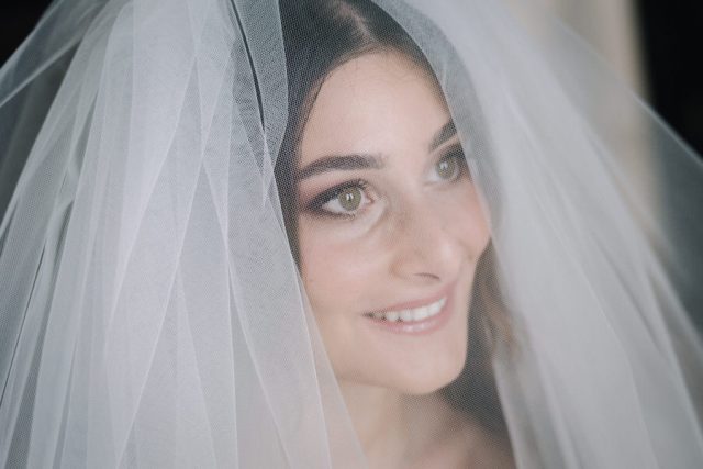 Portrait radieux de la mariée souriant doucement sous son voile de mariée traditionnel.
