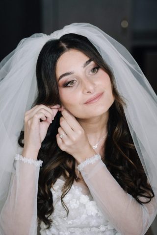 La mariée ajuste délicatement ses boucles d'oreilles lors de sa mise en beauté le jour J.
