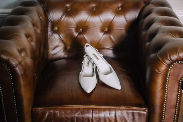 Détail des escarpins blancs de la mariée posés sur un fauteuil en cuir au Château de la Beaumetane