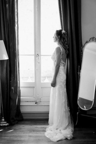 Élégant portrait en noir et blanc de la mariée de profil devant la grande fenêtre.