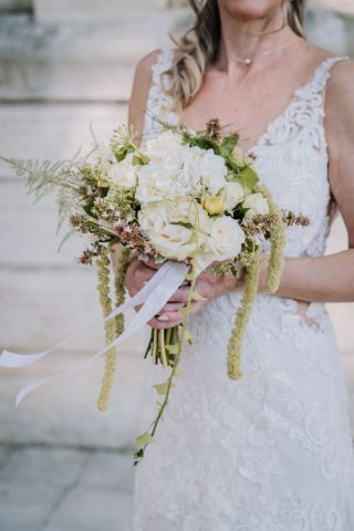 Gros plan sur la mariée souriante tenant son bouquet floral aux tons verts et blancs.