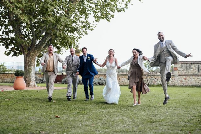 Les mariés courent joyeusement avec leurs témoins dans le grand parc arboré du domaine.