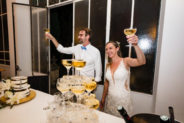 Les mariés lèvent leurs coupes pour trinquer joyeusement derrière leur pyramide de champagne.