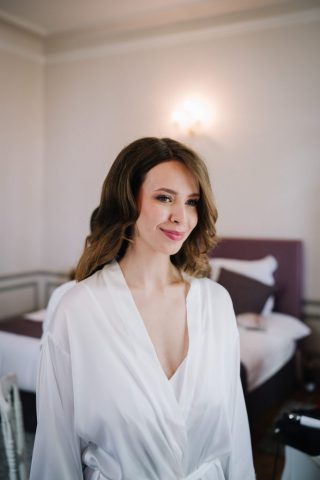 La mariée en peignoir blanc regarde par la fenêtre avec émotion avant de s'habiller.