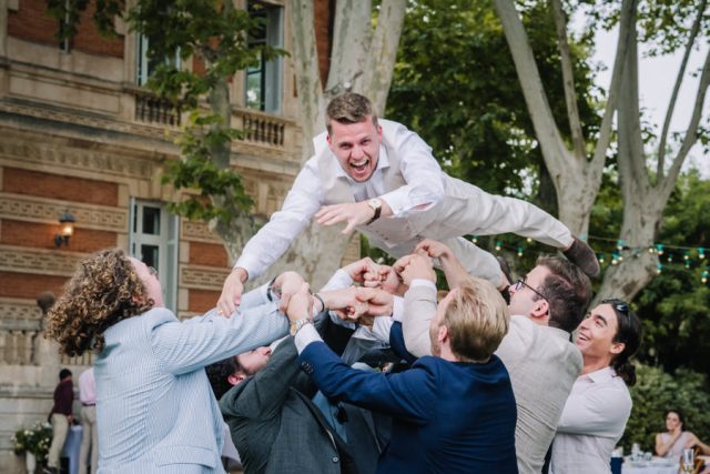 Le marié est lancé en l'air par ses amis dans une ambiance festive au domaine de réception.