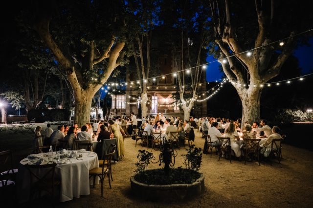 Les longues tables de banquet illuminées la nuit dans le parc du lieu de réception.