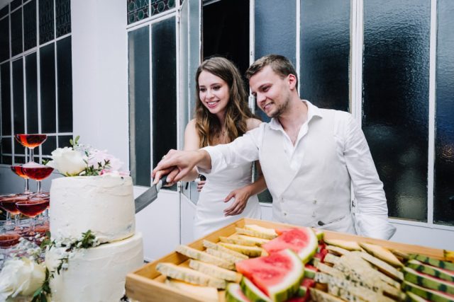 Les jeunes mariés découpent leur wedding cake entourés d'un grand buffet de fruits.