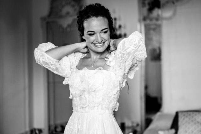 Portrait radieux de la mariée souriante ajustant ses cheveux lors de ses préparatifs (Noir et blanc).