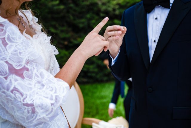 Gros plan sur le marié glissant l'alliance au doigt de la mariée sous la Houppa.