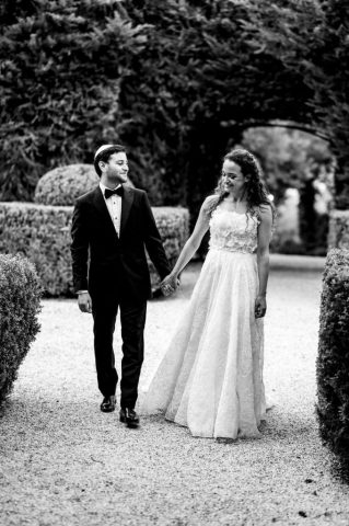 Promenade romantique des jeunes mariés dans les magnifiques jardins du domaine en noir et blanc.