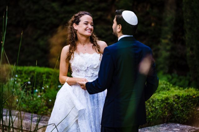 Le marié, portant la kippa, regarde amoureusement sa femme dans le parc verdoyant du domaine.