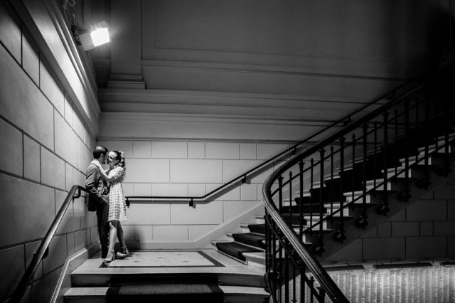 Baiser romantique du couple sur le majestueux grand escalier de la mairie parisienne en noir et blanc.
